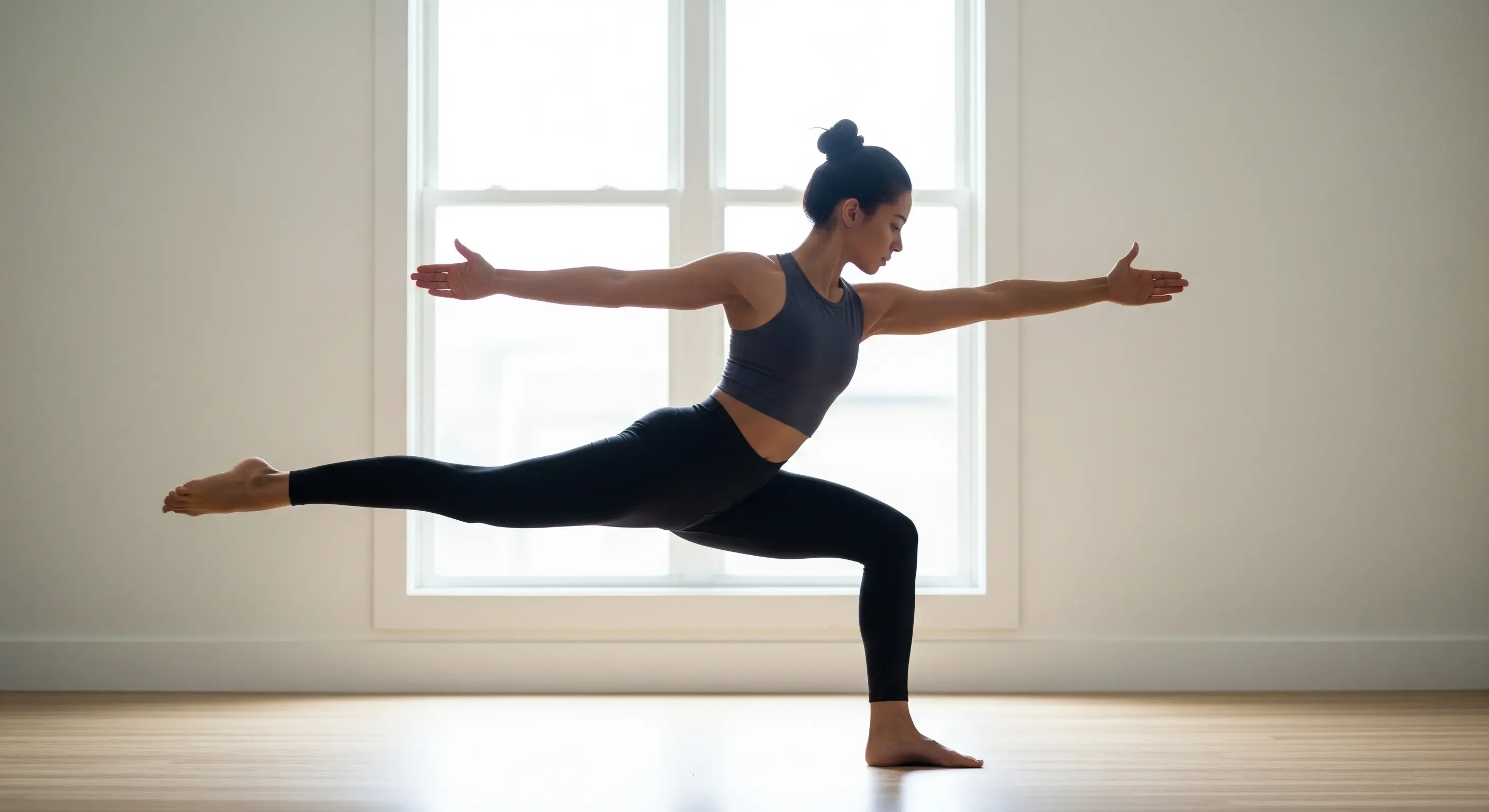 Donna in equilibrio nella posizione yoga del Guerriero III (Virabhadrasana III) in una stanza luminosa, che dimostra l'aumento della forza del core e delle gambe e l'equilibrio fisico.