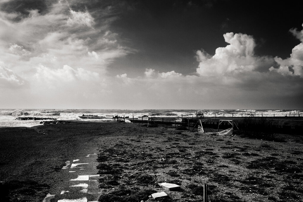 Spiaggia di Ostia battuta dal vento con il mare agitato sullo sfondo e un ampio cielo carico di nuvole. Fotografia di Antonio Crialesi. - Wind-swept beach in Ostia with rough seas in the distance beneath a vast cloud-filled sky. Photograph by Antonio Crialesi.
