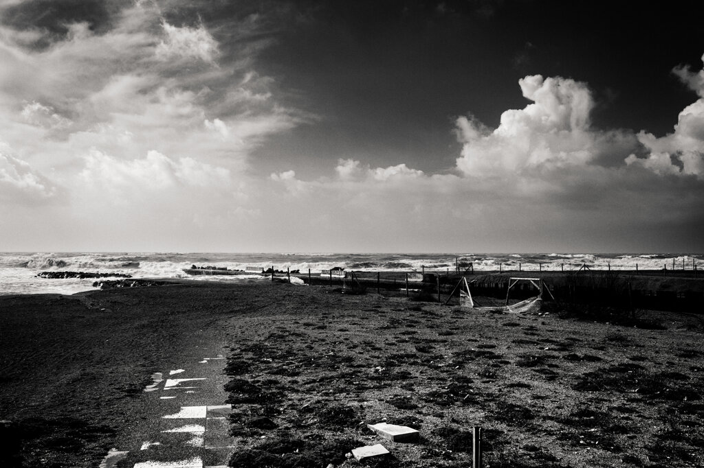 Spiaggia vuota a Ostia, con il mare agitato dal vento sotto un cielo carico di nuvole. - Empty beach in Ostia, with the wind-whipped sea beneath a cloud-laden sky.