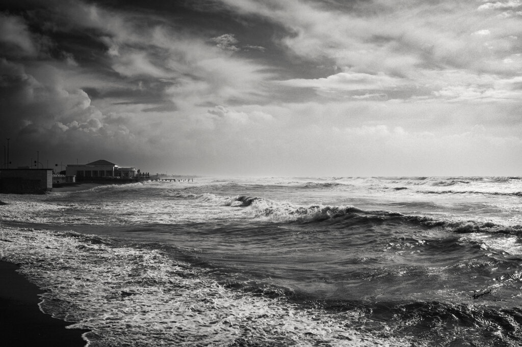 Mare agitato sotto un cielo ancora carico di pioggia, con uno stabilimento balneare sullo sfondo a Ostia. - Rough sea beneath a rain-heavy sky, with a beach club in the background in Ostia.