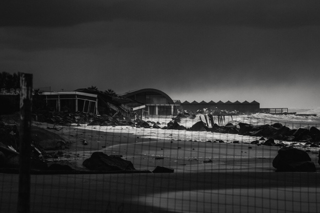 Stabilimento balneare in rovina oltre una recinzione, sul mare in tempesta a Ostia. - Derelict beach club beyond a fence, set against the stormy sea in Ostia.