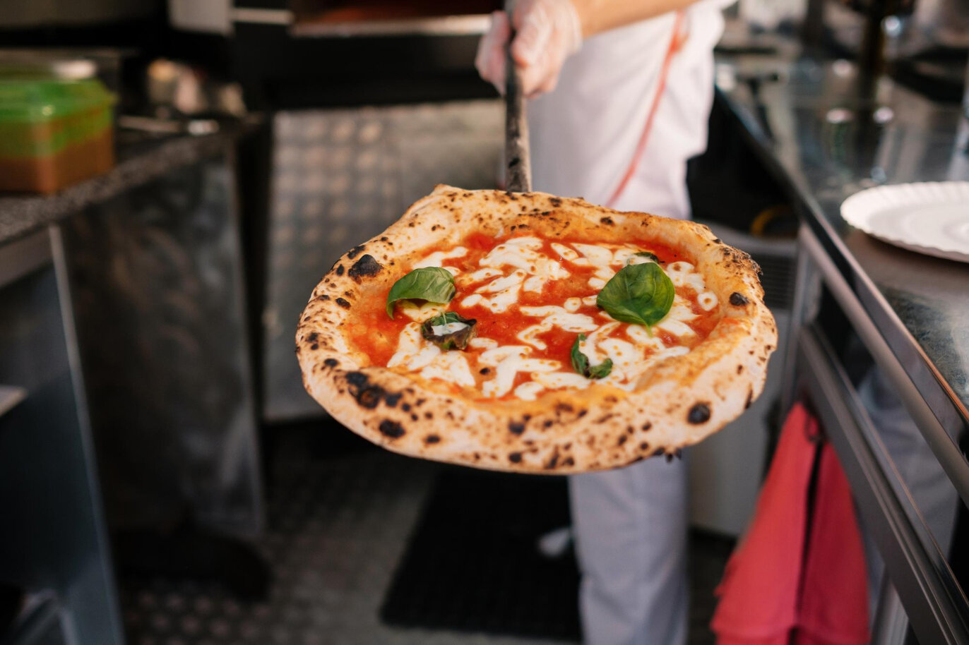 the-process-of-making-pizza-the-cook-shows-the-pizza-that-he-got-out-of-a-woodfired-oven-street-food-cooking-concept.jpeg