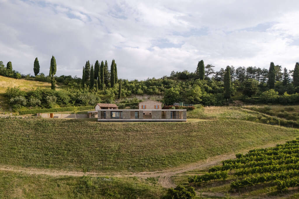 Vista del fronte verso valle con grande terrazza e ampliamento contemporaneo integrato nel pendio, Romagna 