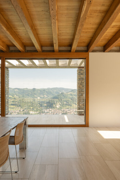 Zona living con pavimento in travertino a correre e grandi vetrate sul paesaggio collinare, Effevu House