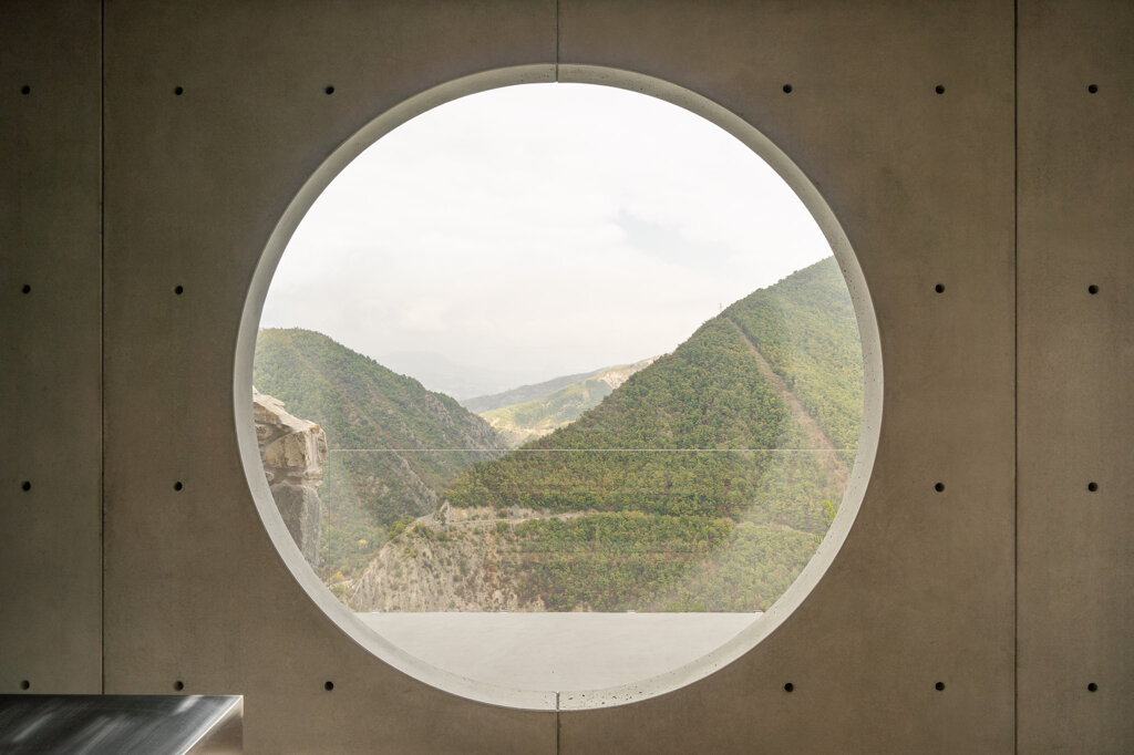 Finestra circolare di cemento con vista sui meandri del Trebbia, omaggio a Carlo Scarpa