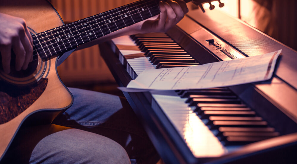 uomo-che-suona-la-chitarra-acustica-e-il-piano-in-primo-piano-note-di-registrazione-bel-colore-di-sfondo-concetto-di-attivita-musicale.jpeg