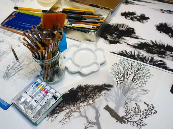 Artisan workspace of the Balbusso Twins with hand-drawn clouds and trees on tracing paper, surrounded by traditional painting tools, gouache tubes, and brushes. Artisan workspace of the Balbusso Twins with hand-drawn clouds and trees on tracing paper, surrounded by traditional painting tools, gouache tubes, and brushes.