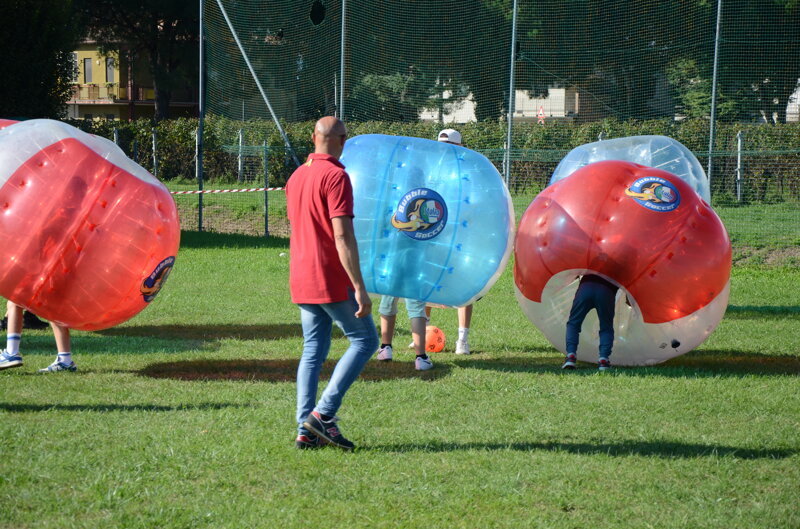 ragazzi che rincorrono la palla su un prato con le bolle di bubble soccer all'evento Ecogiochiamoa a Busiago