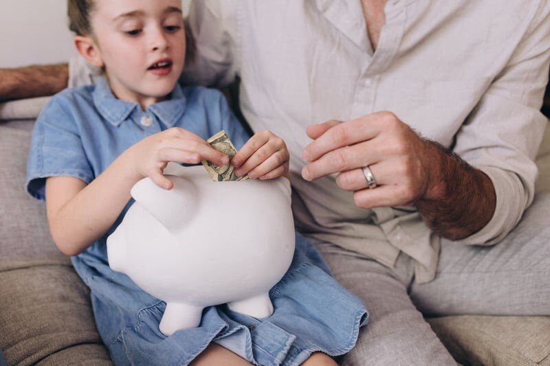 una bambina mette dei soldi nel salvadanaio aiutata dal papà