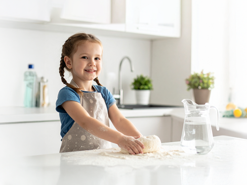 Bambina che impasta con una caraffa d'acqua a fianco in una cucina bianca moderna
