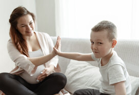 ragazzino-di-alta-cinque-alla-mamma-incinta-seduta-sul-divano-casa.jpeg