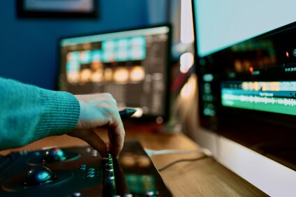 mano che regola i comandi di una console di color grading davanti a due monitor di montaggio video