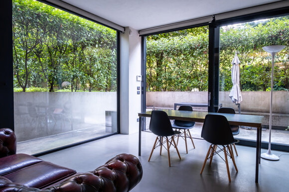 sala da pranzo moderna con grandi vetrate sul giardino e tavolo con sedie nere