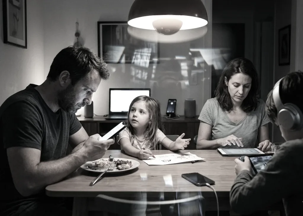 mentre cenano genitori con smartphone, figlio con cuffie e figlia piccola disegna rivolgendosi al padre