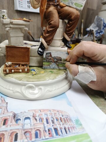 Artigiano che dipinge a mano una miniatura del Colosseo su una statuina in porcellana di Capodimonte firmata Carusio.