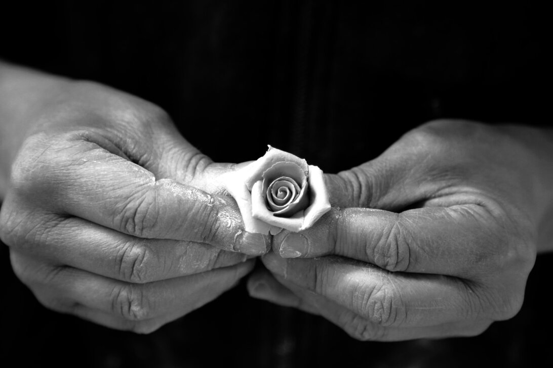 Mani sapienti creano un fiore in porcellana di Capodimonte, simbolo della maestria artigianale di Porcellane Carusio