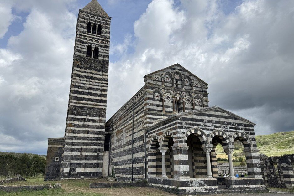 basilica-saccargia-sardegna-sassari-villa-malvasio.jpeg Fotografia diurna reale della facciata e del campanile della Basilica di Saccargia a Codrongianos. L’immagine mostra la caratteristica architettura romanica bicroma a strisce bianche e nere contro un cielo azzurro limpido.