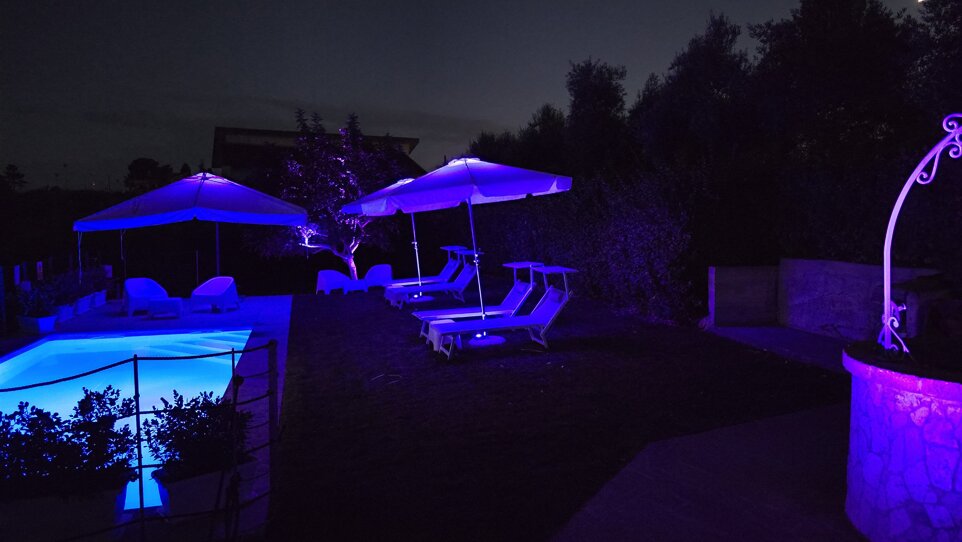 Illuminated swimming pool with blue lights and parasols for evening events at Villa Malvasio Sassari