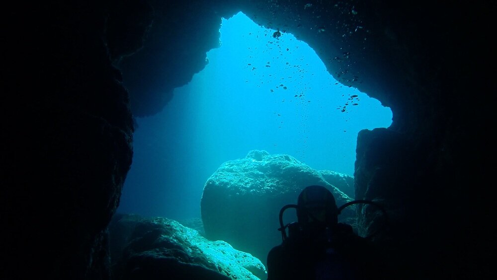 grotte-sommerse-alghero-immersioni-sardegna.jpeg Suggestivo scorcio dall'interno di una grotta marina sommersa ad Alghero, tra le bolle dei subacquei e l'acqua azzurra e cristallina.