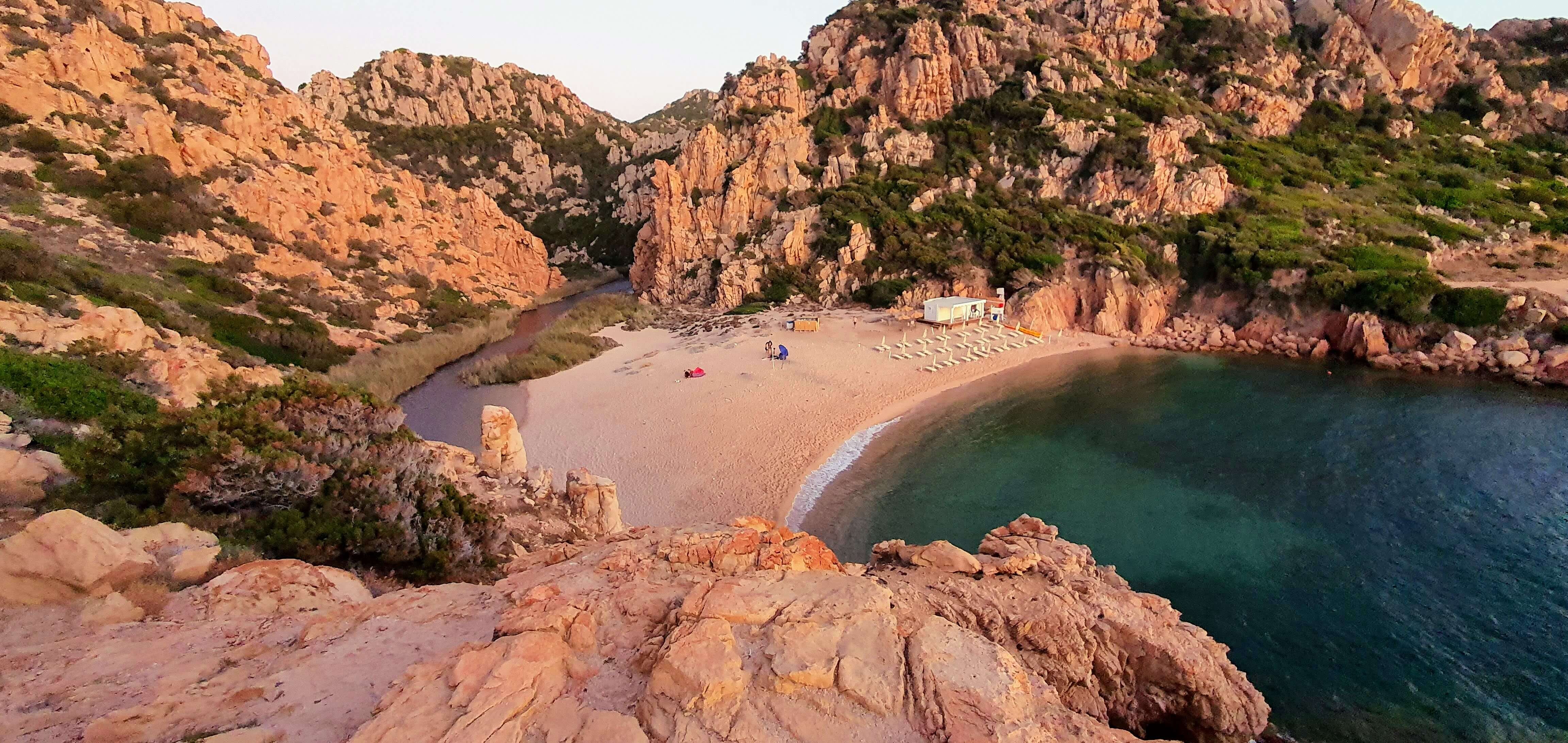 spiaggia-li-cossi-trachite-rossa-costa-paradiso.jpeg Spiaggia di Li Cossi a Costa Paradiso circondata da rocce di trachite rossa.