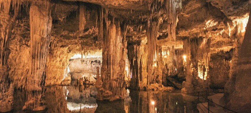 nterno spettacolare delle Grotte di Nettuno ad Alghero, con il suggestivo Lago sotterraneo Lamarmora illuminato, circondato da antiche stalattiti e imponenti formazioni carsiche.