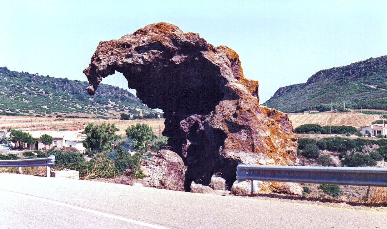 roccia-dell-elefante-castelsardo-sassari.jpeg Fotografia reale della Roccia dell’Elefante a Castelsardo, monumento naturale e archeologico di trachite color ruggine erosa dal vento. L’inquadratura evidenzia la forma che ricorda un pachiderma seduto a bordo strada.