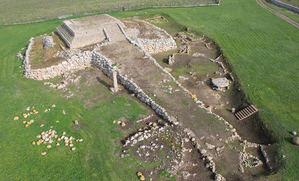 Fotografia aerea del santuario prenuragico di Monte d'Accoddi, vicino a Sassari. La veduta dall'alto mostra chiaramente l'altare monumentale a gradoni e la lunga rampa d'accesso unica nel Mediterraneo, circondata dalla campagna sarda