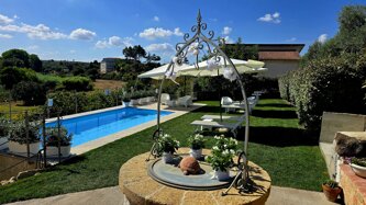 Daytime view of the garden with stone well and swimming pool with parasols at Villa Malvasio