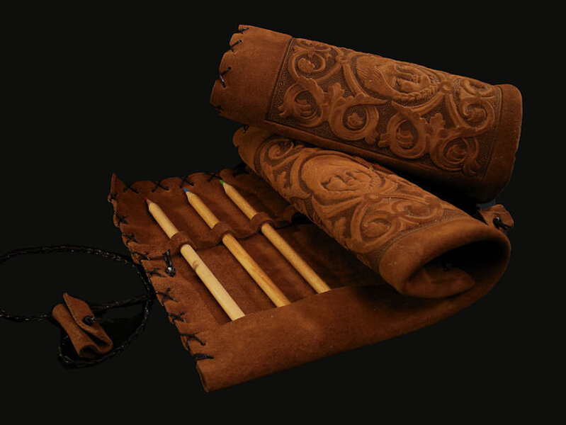 Contenitore portamatite di pelle visto aperto con le matite esposte e chiuso arrotolato messo sopra