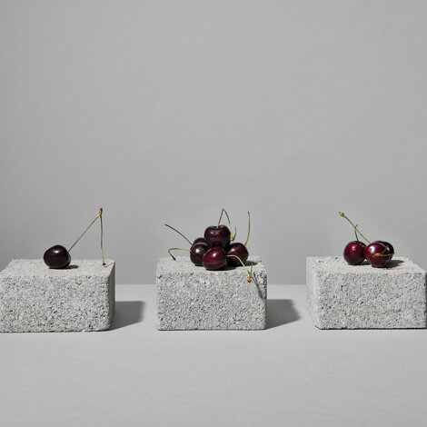 Still life di ciliegie adagiate su tre piccoli blocchi grigi