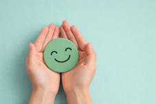 Mani che sorreggono uno smile verde su sfondo azzurro, simbolo di equilibrio. Percorso di dieta e sana alimentazione a Bolzano con la Dott.ssa Erica Roccatello nutrizionista, per ritrovare il benessere generale e l'energia quotidiana.