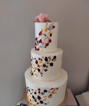 Torta bianca a piani con petali di fiore e disegni a mano 