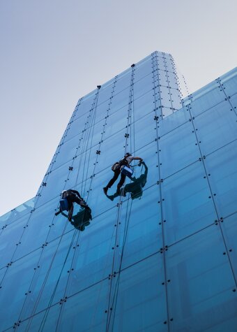 vertical-low-angle-shot-two-people-climbing-tall-glass-building-day-time.jpeg