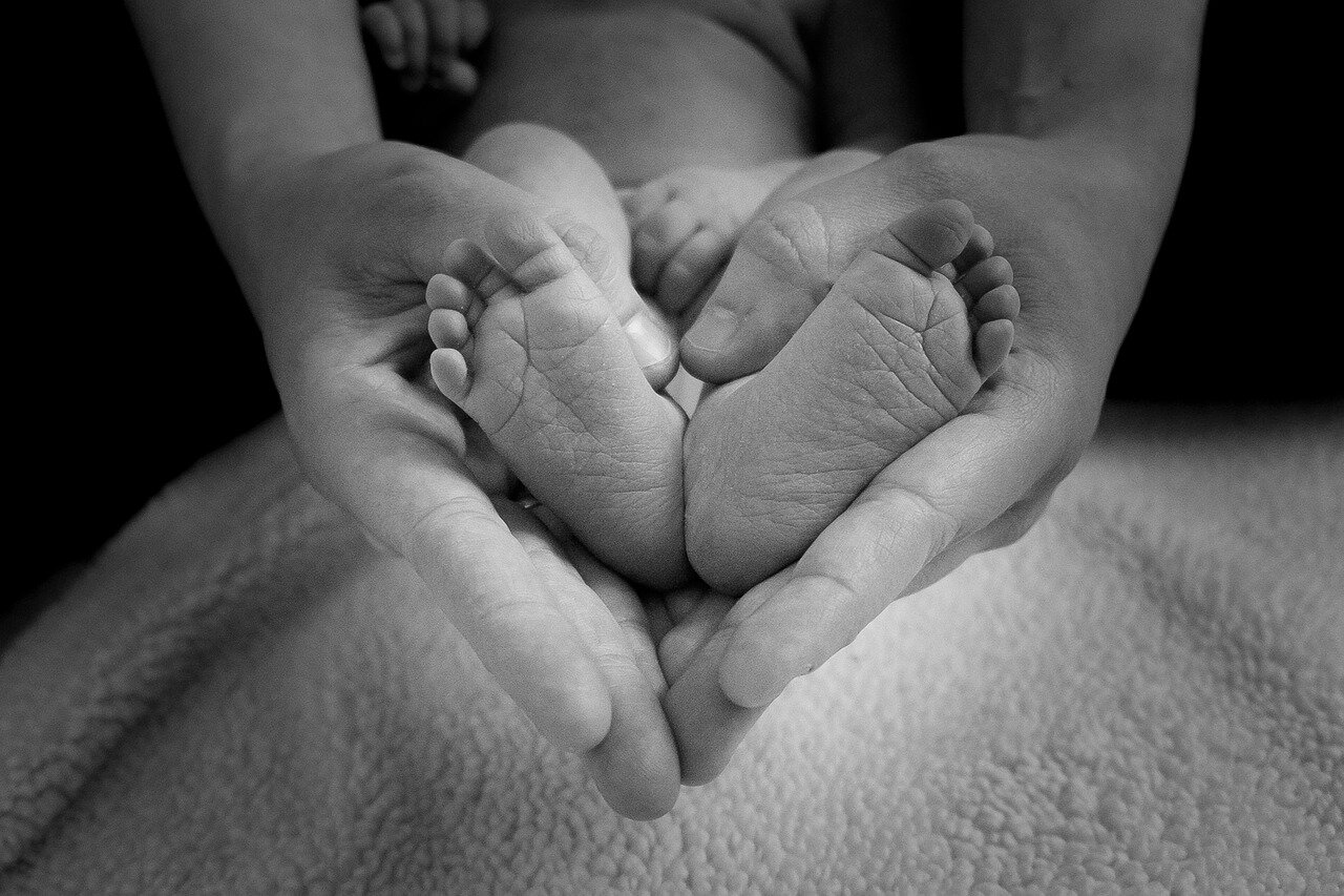 Gravidanza e parto con i Fiori di Bach Mani che stringono i piedini di un neonato, foto in bianco e nero.