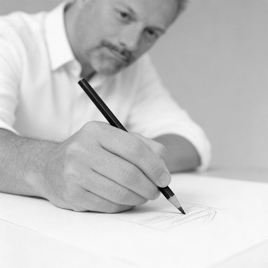 Ritratto in bianco e nero di Federico Ottavio Barberis, fondatore di BFO Stile, seduto a una scrivania che impugna una matita da disegno in procinto di disegnare delle forme geometriche.