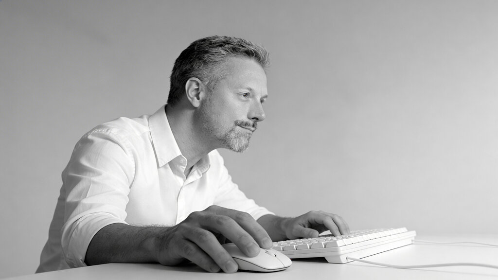 Ritratto in bianco e nero di Federico Ottavio Barberis, fondatore di BFO Stile, seduto a una scrivania che utilizza tastiera e mouse intento a lavorare..