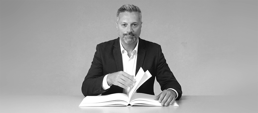 eyJpdCI6IkJhcmJlcmlzIEZlZGVyaWNvIE90dGF2aW8gc2VkdXRvIGFkIHVuYSBzY3JpdmFuaWEgY2hlIHNmb2dsaWEgdW4gbGlicm8gYmlhbmNvIGFwcG9nZ2lhdG8gc3VsIHRhdm9sby4gSW1tYWdpbmUgY2hlIGRlc2NyaXZlIGxhIHZvbG9udOAgZGkgbW9zdHJhcmUgaWwgcmlzdWx0YXRvIGRlbCBwcm9wcmlvIGxhdm9yby4ifQ==