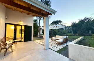 Vista della villa con ampio giardino mediterraneo e prato.