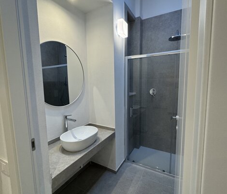 Bagno moderno con ampia doccia, lavabo e finiture chiare.