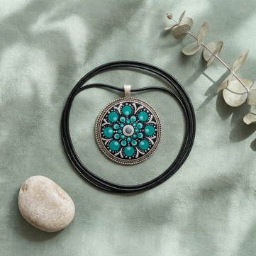 Pendente circolare turchese, realizzato con la tecnica della dot art, fotografato su una superficie chiara con elementi naturali intorno. Pendente circolare turchese, realizzato con la tecnica della dot art, fotografato su una superficie chiara con elementi naturali intorno.