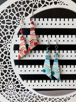 Due paia di orecchini pendenti decorati con motivi dot art nei colori rosso e bianco e turchese e bianco, fotografati su un supporto decorativo bianco. Due paia di orecchini pendenti decorati con motivi dot art nei colori rosso e bianco e turchese e bianco, fotografati su un supporto decorativo bianco.