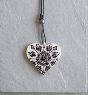 pendente a cuore bianco e nero, con decorazione puntinata molto grafica e simmetrica, fotografato su una superficie effetto pietra.
