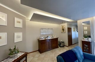 Soggiorno tinteggiato nei toni del tortora e beige chiaro, con controsoffitto moderno a pannelli illuminati a LED 