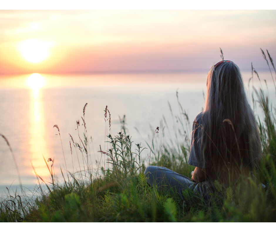 Cortisolo: amico esuberante o nemico silenzioso? tramonto, donna seduta nella natura, mare, erba e fiori, colori rilassanti
