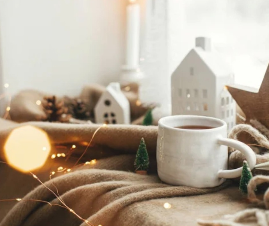 Hygge non è ciò che vedi, è ciò che senti Tazza calda davanti a una finestra invernale con casette illuminate, atmosfera hygge di calore interiore