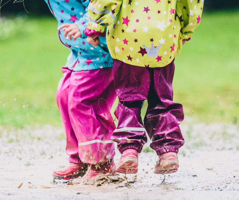 Due bambini giocano saltando nelle pozzanghere con abiti colorati, simbolo della curiosità e della libertà in stile Hygge.