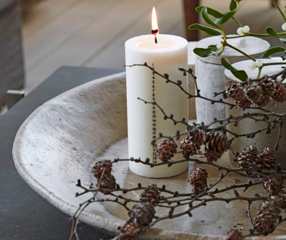 candela kalenderlys accesa con numeri dell’Avvento, ramo naturale e decorazioni hygge su un vassoio