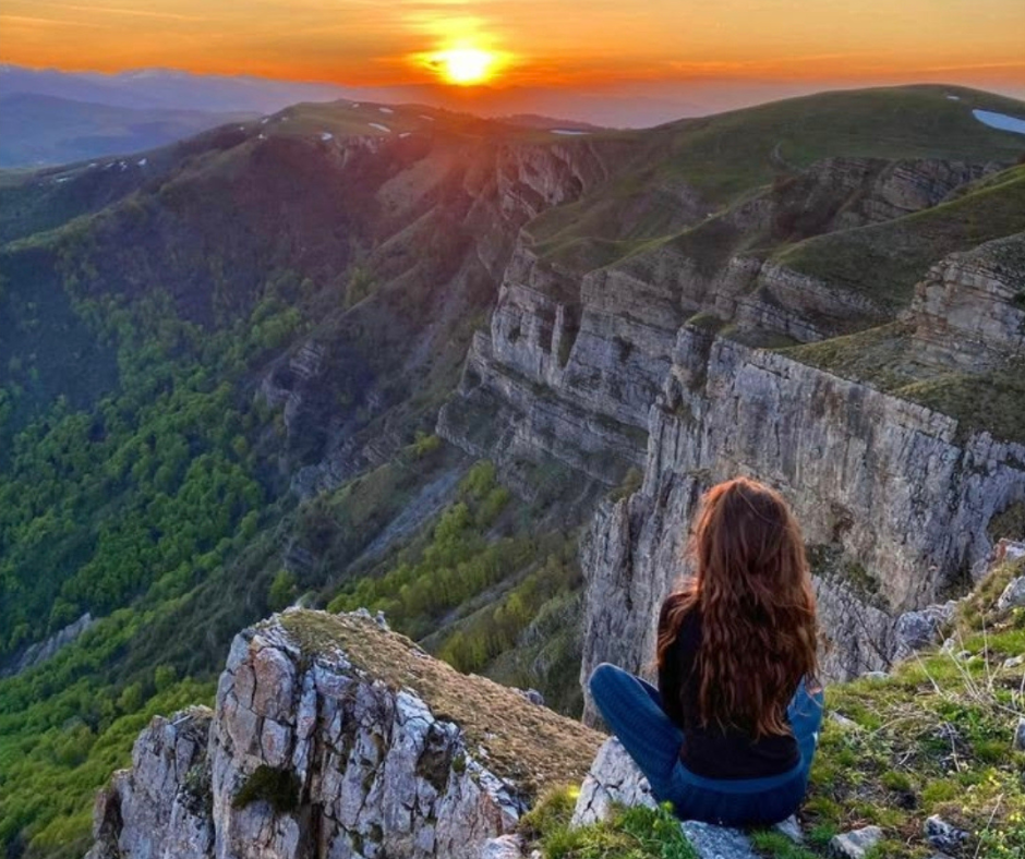 Donna seduta su una montagna che osserva l'orizzonte simbolo della ricerca dei propri valori e della direzione nella vita