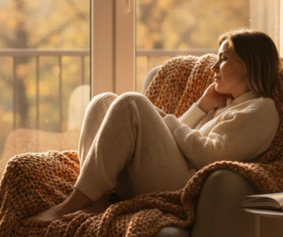 Quando lo stress non è più solo un momento Donna seduta su una poltrona vicino alla finestra con espressione riflessiva simbolo di stress cronico e stanchezza mentale in stile hygge