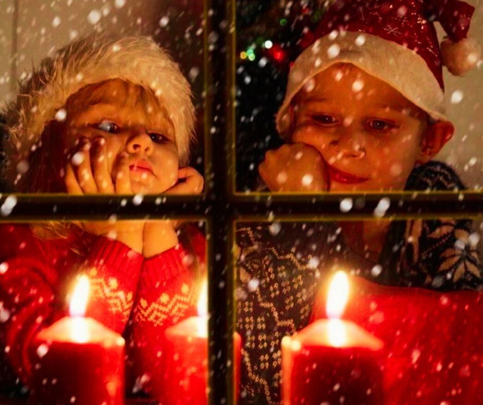 bambini che guardano fuori dalla finestra con candele accese aspettando il Natale in stile hygge